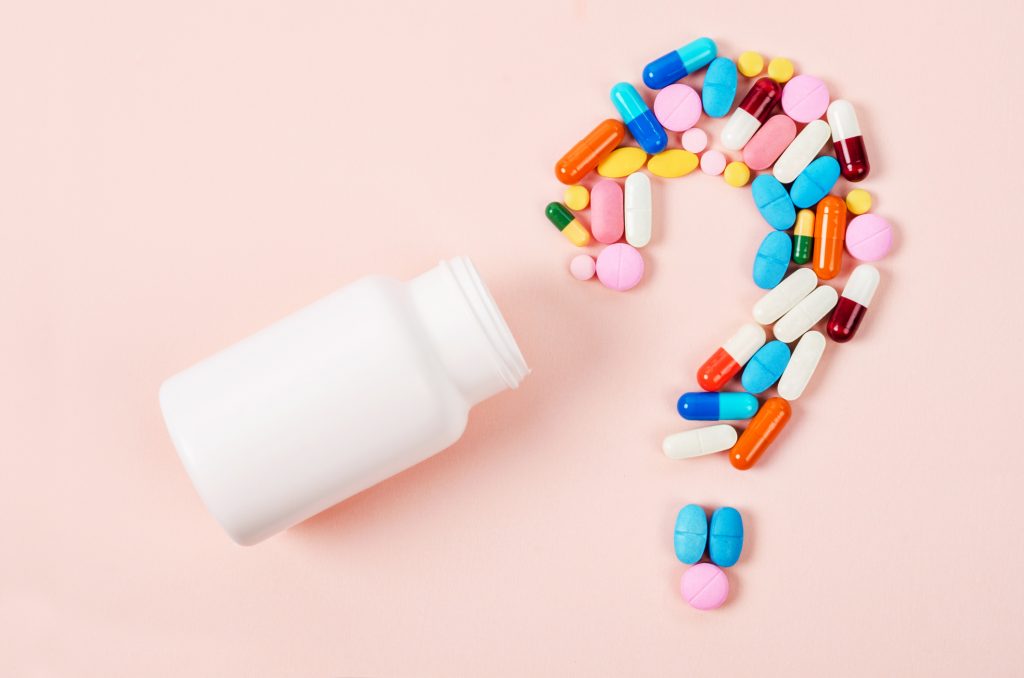 Close-up of open pill bottle with a variety of pills forming a question mark