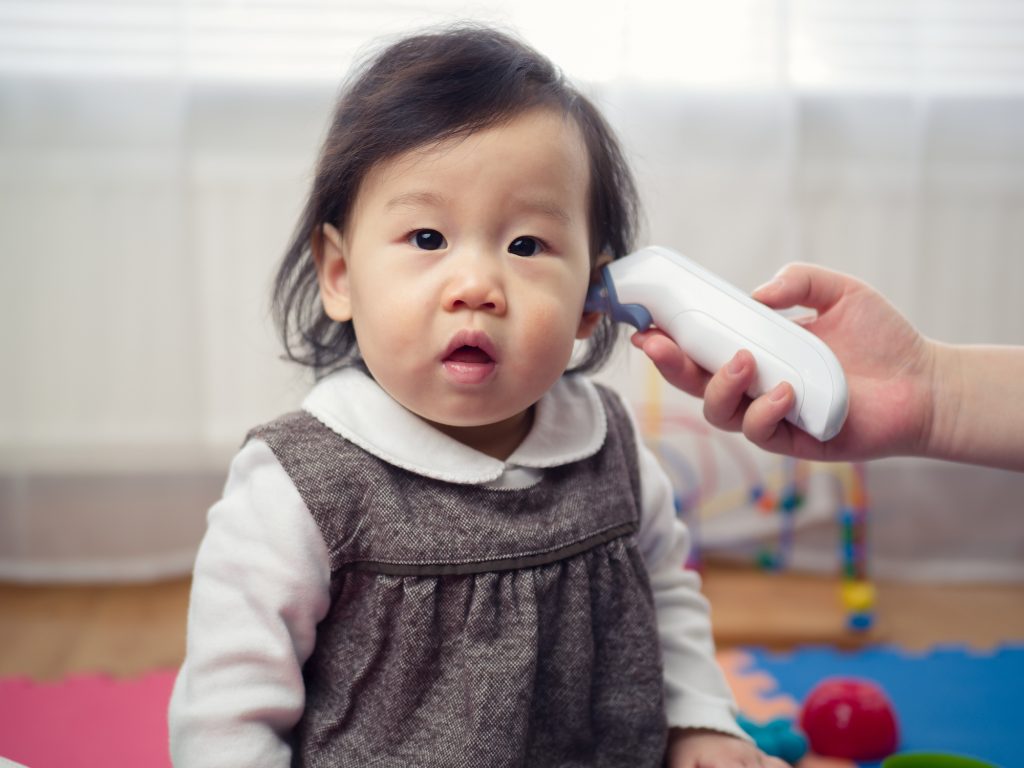 Close-up of a small child with an adult holding a digital thermometer to their ear.