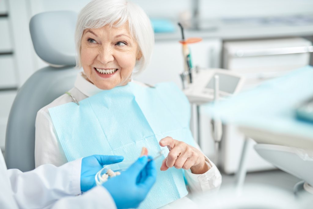 An older adult sits in a dentist's chair with bib on, speaking with dental professional out of shot.
