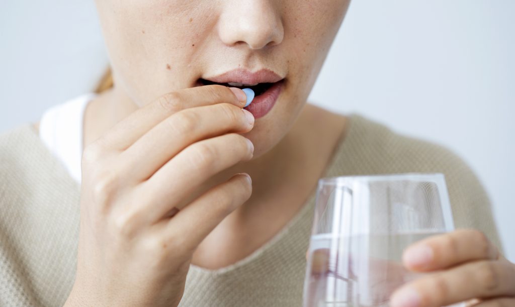 Close up of person taking a pill while holding a glass of water.