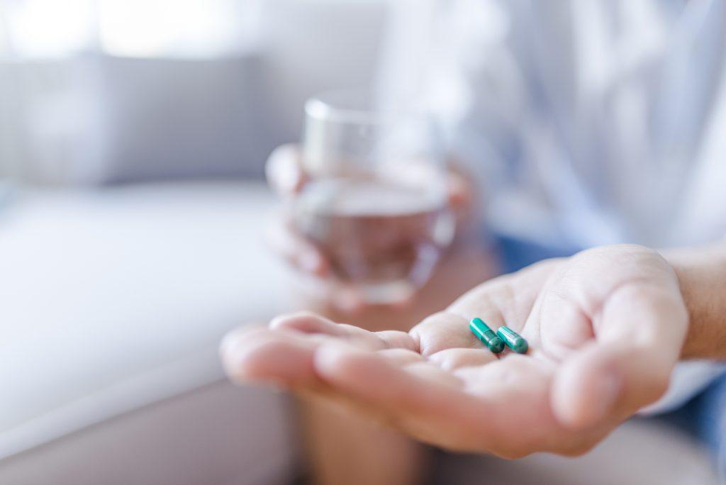 Close-up of open hand with two antibiotics and a glass of water