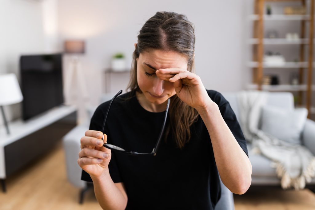 A woman holding glasses and rubbing eyes.